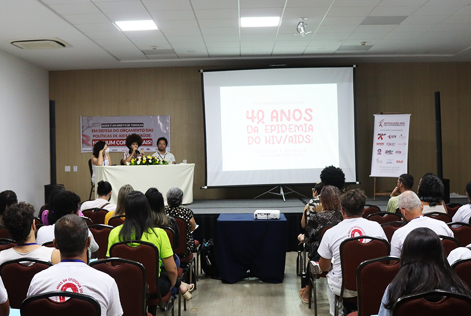 auditório com dezenas de pessoas sentadas de costas olhando para participantes de uma mesa no 1º seminário estadual de HIV/AIDS em Pernambuco